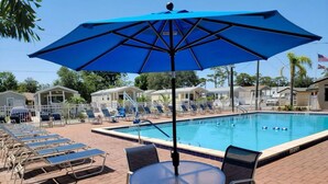 A swimming pool area with lounge chairs, a table, and an umbrella. - Family-Friendly Cottage Near Disney with Pool, Playground & Resort Amenities (Kissimmee)