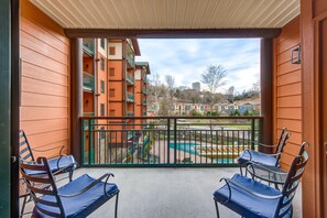 A balcony with two lounge chairs, a view of a swimming pool, and a building with multiple balconies in the background. - Baskins Creek 208 (Gatlinburg)