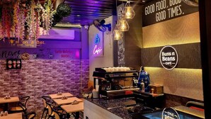 A restaurant interior with exposed brick walls, hanging plants, and a counter displaying buns and beans. - CHERRY TREE (Greater Noida)