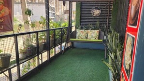 A balcony with artificial grass, a hanging chair, and a wall-mounted sign. - CHERRY TREE (Greater Noida)