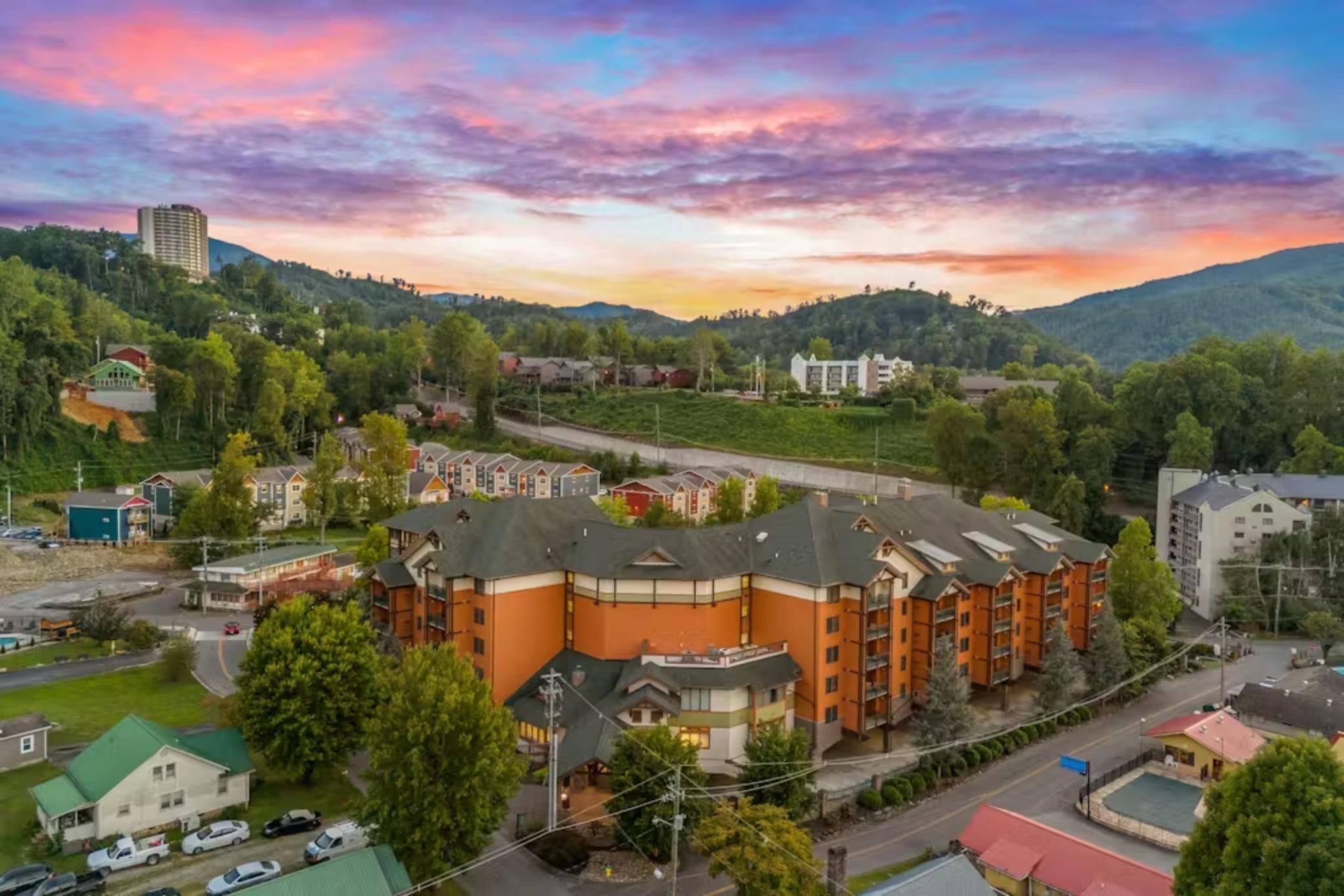 A multi-story hotel with a central courtyard, surrounded by greenery and a hilly landscape.