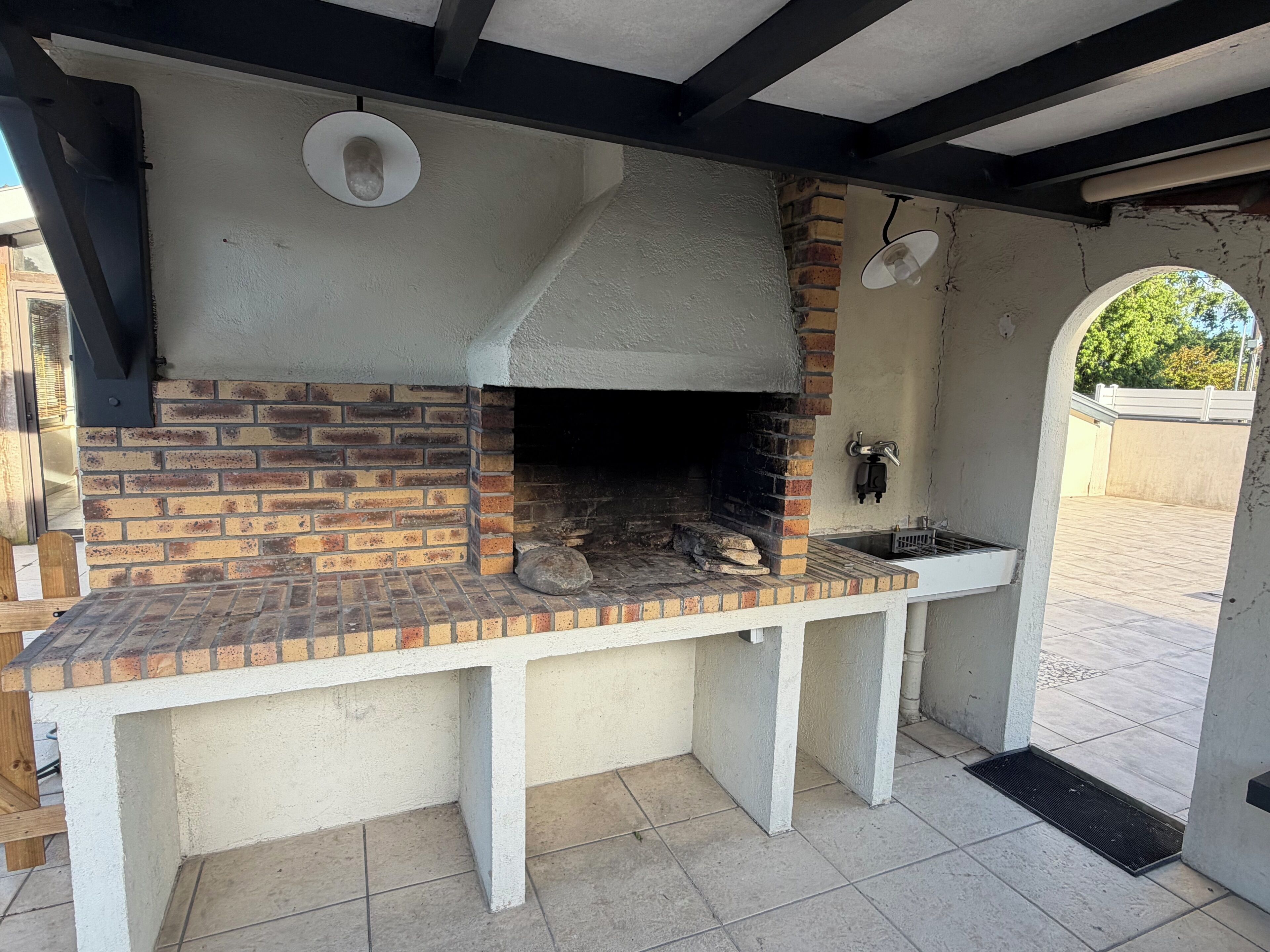 Cocina al aire libre de ladrillo con chimenea, un lavaplatos y una ventana.