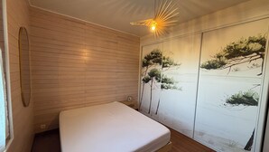 Een slaapkamer met een houten vloer, een bed, een plafondventilator en een muur met een natuurdecoratie.