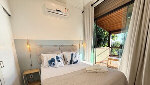 Camera da letto con un letto, un comodino, un condizionatore e vista sul verde attraverso una porta in vetro.