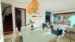 Een moderne woonkamer met een glazen eettafel, blauwe banken en een groot raam met uitzicht op het groen.