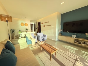 Ein modernes Wohnzimmer mit einer Couch, Sesseln, einem Couchtisch, einem Fernseher und einer Treppe, die in eine weitere Ebene führt.