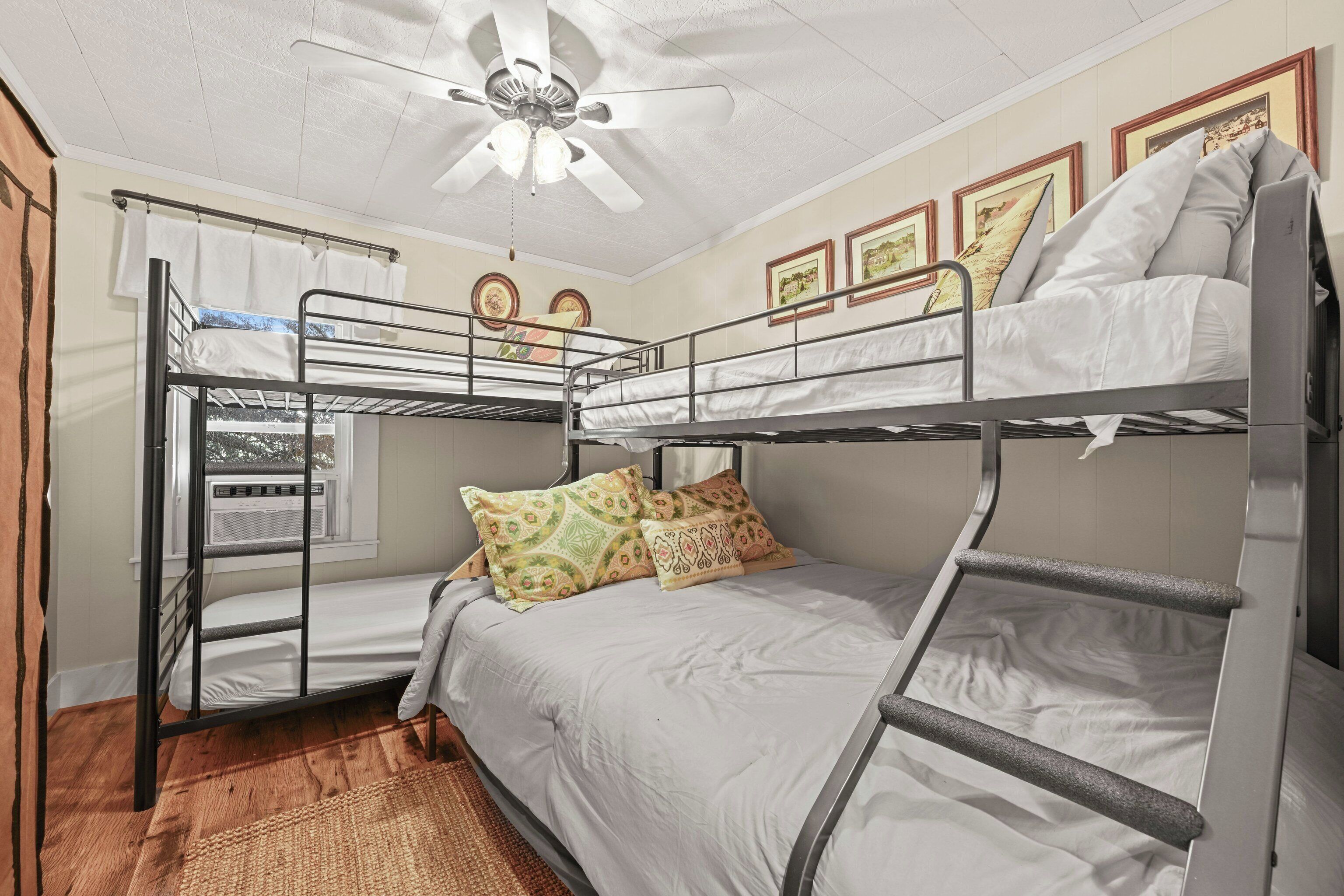 Habitación con literas, ventilador de techo, cuadros en la pared y ventana con cortinas.