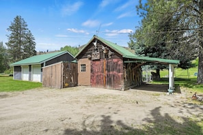 A rustic barn with a green roof, a covered porch, and a small adjacent shed.