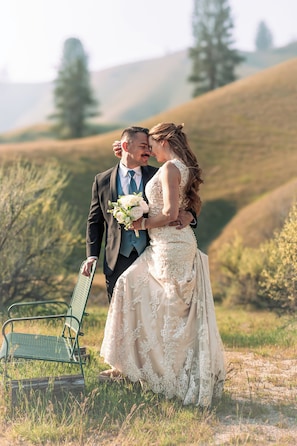 A couple embracing in a field with a green bench and a chair.