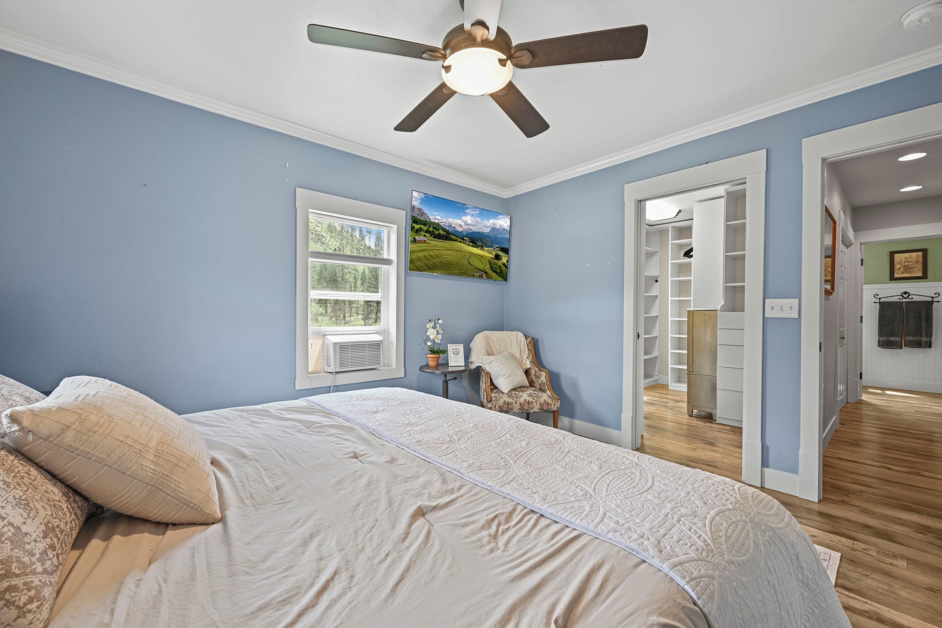 Un dormitorio con cama, ventilador de techo, ventana, una silla y vestidor.