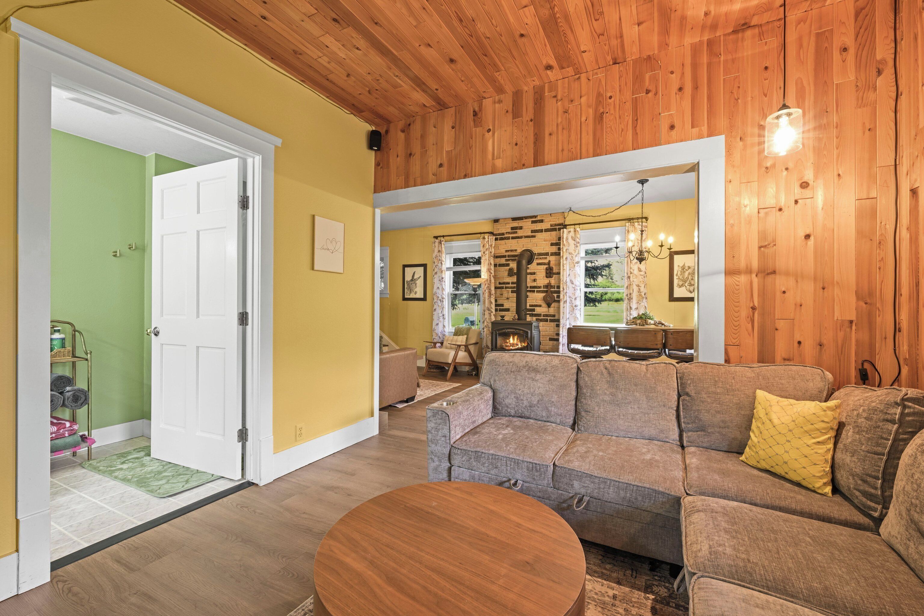 A living room with a wooden ceiling, a green wall, a beige sofa, and a round wooden table.