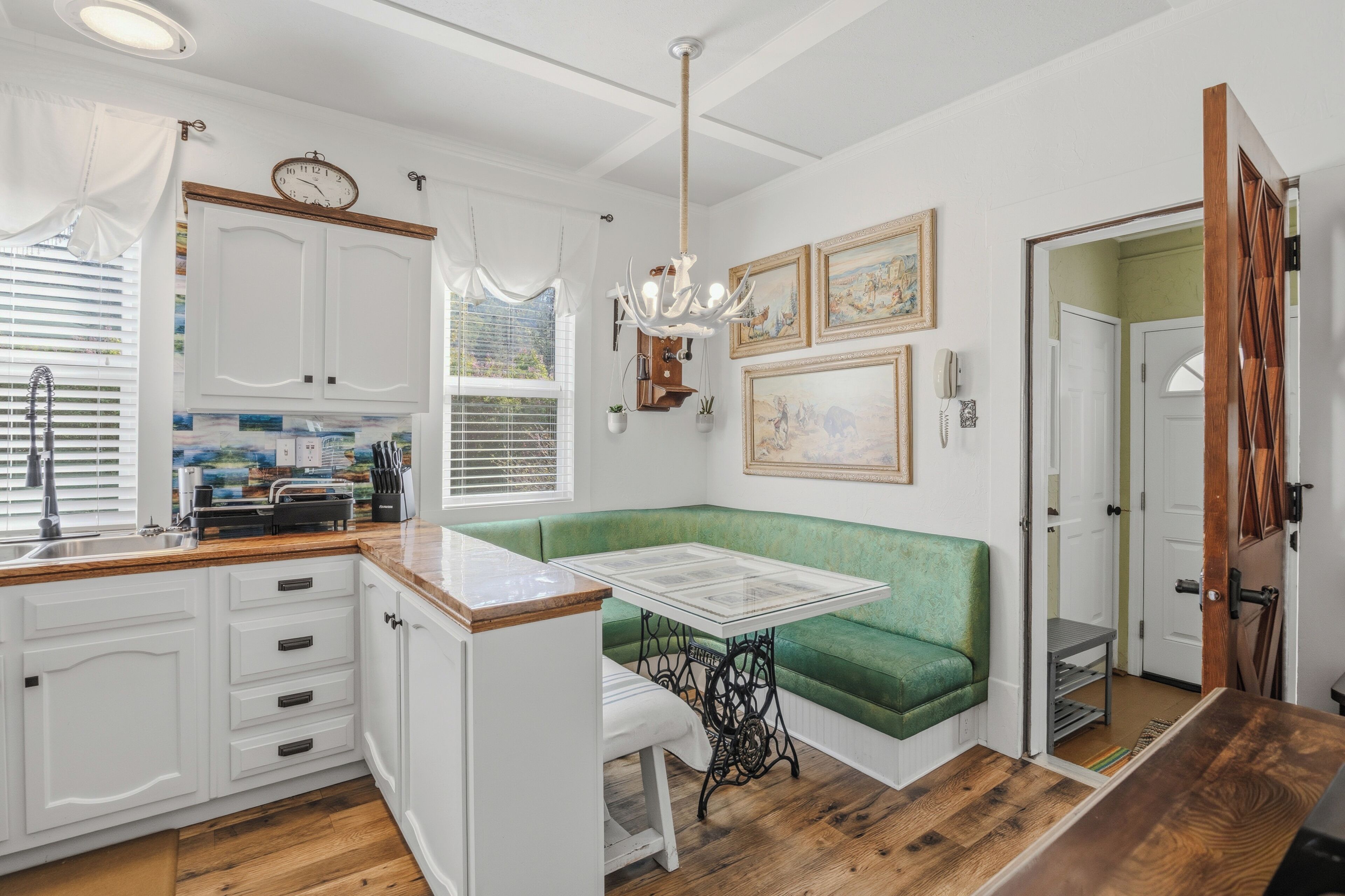 A kitchen with white cabinets, a green bench, a table, and a chandelier.