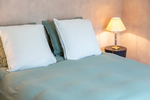 A bed with a light blue bedspread, two pillows, and a bedside lamp on a round table. - Bed and Breakfast 'Une Chambre À Lestriguiou' with Private Terrace, Private Garden and Wi-Fi (Plomeur)