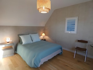 Une chambre à coucher comprenant un lit, des tables de chevet, une chaise, un luminaire suspendu et un tableau encadré accroché au mur.