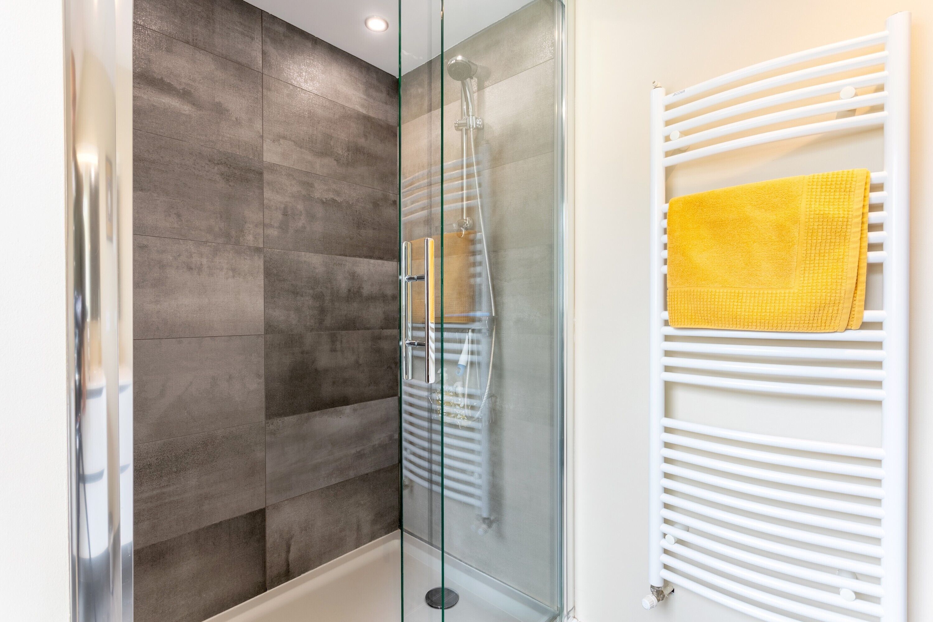 Un bagno moderno con box doccia in vetro, un termosifone bianco e un asciugamano giallo.