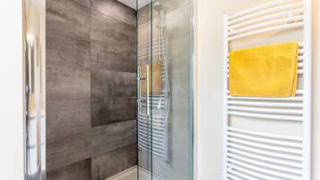 Un bagno moderno con box doccia in vetro, un termosifone bianco e un asciugamano giallo.