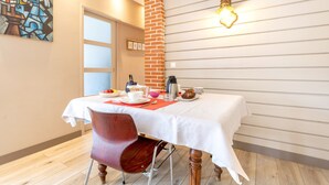 A dining area with a table set for two, a red chair, a white tablecloth, and a brick column. - Bed and Breakfast 'Une Chambre À Lestriguiou' with Private Terrace, Private Garden and Wi-Fi (Plomeur)