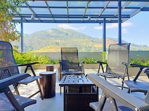 A covered outdoor seating area with chairs and tables, overlooking a mountainous landscape.