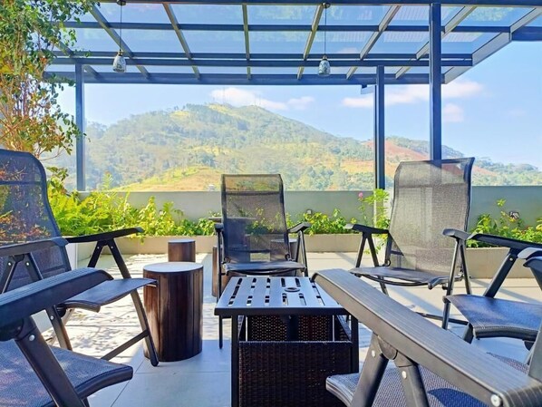 A covered outdoor seating area with chairs and tables, overlooking a mountainous landscape.