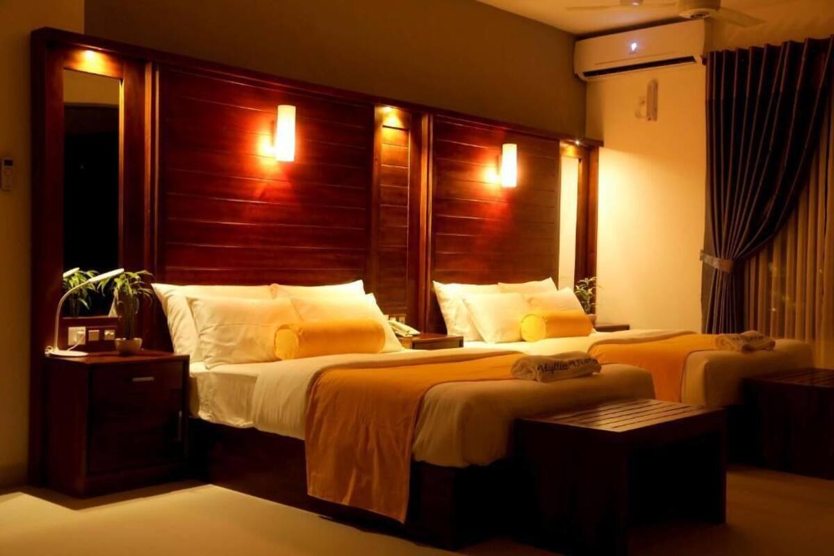 A hotel room with a large bed, two bedside tables, a small sofa, a wooden headboard, and a mirror.