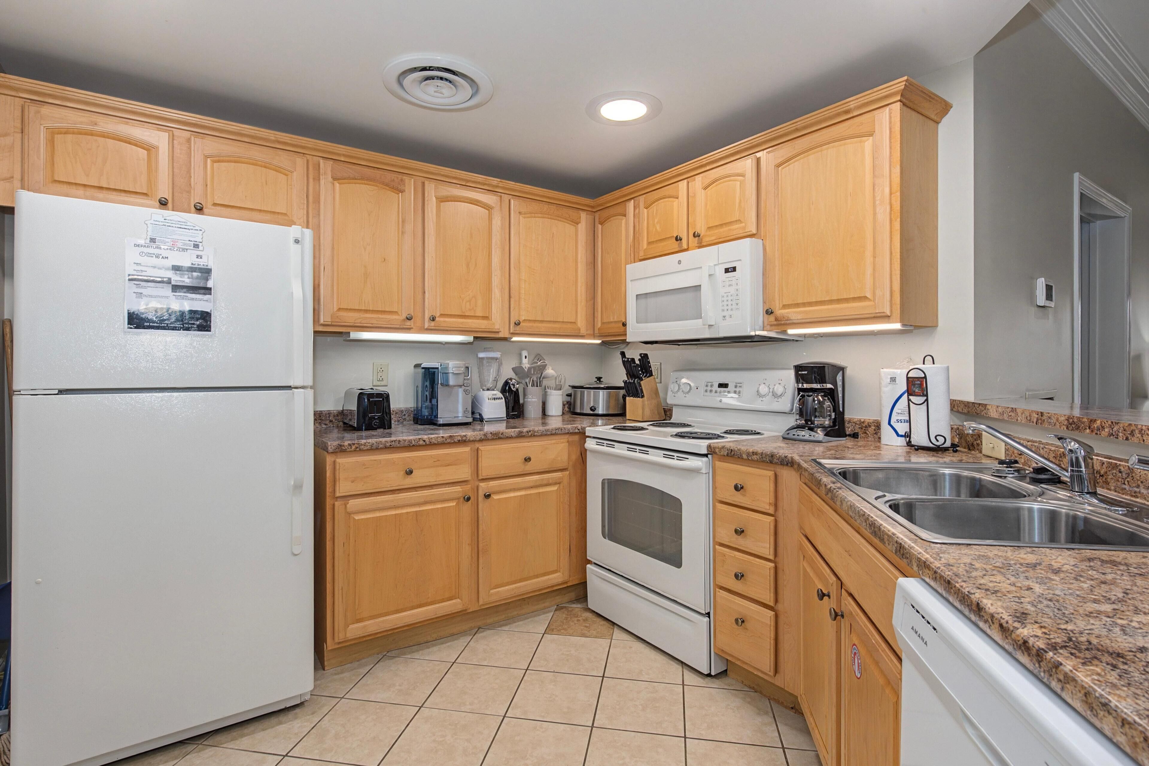 A kitchen with wooden cabinets, a white refrigerator, a microwave, an oven, a dishwasher, and a granite countertop.