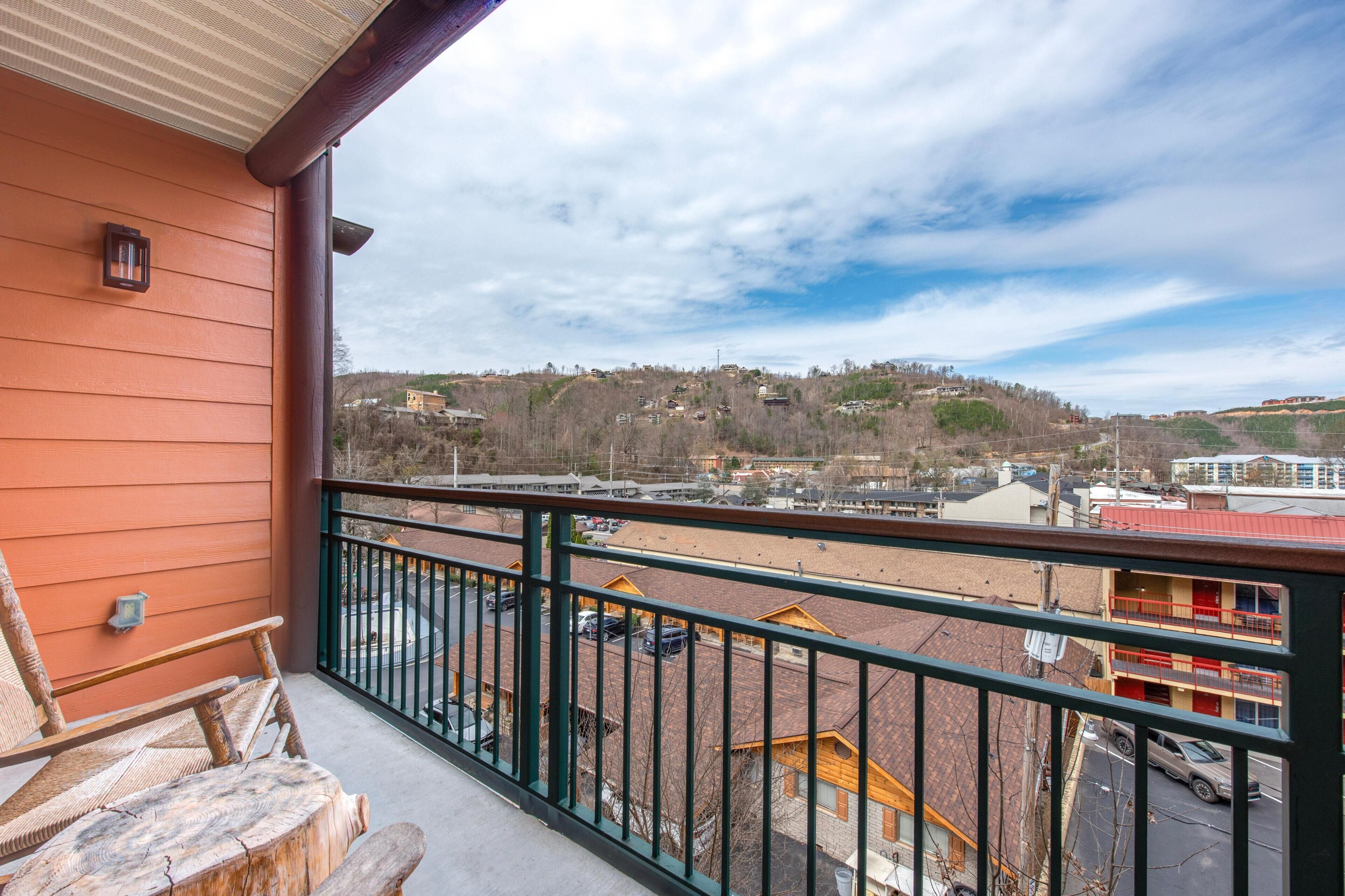 A balcony with a view of a hilly town, a wooden bench, and a railing.
