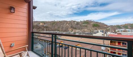 A balcony with a view of a hilly town, a wooden bench, and a railing.