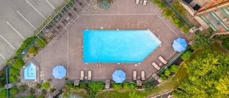 Vista aérea de una piscina rodeada de follaje y sillones de descanso.