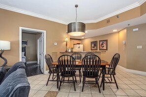 A dining area with a wooden table and chairs, a pendant light, and a kitchen in the background. - Baskins Creek 303 (Gatlinburg)