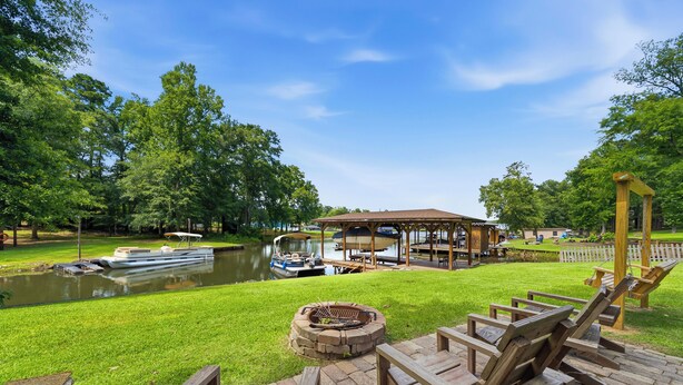 Une terrasse au bord du lac, avec des chaises en bois, un foyer et un belvédère offrant une vue sur un lac paisible où naviguent des bateaux.