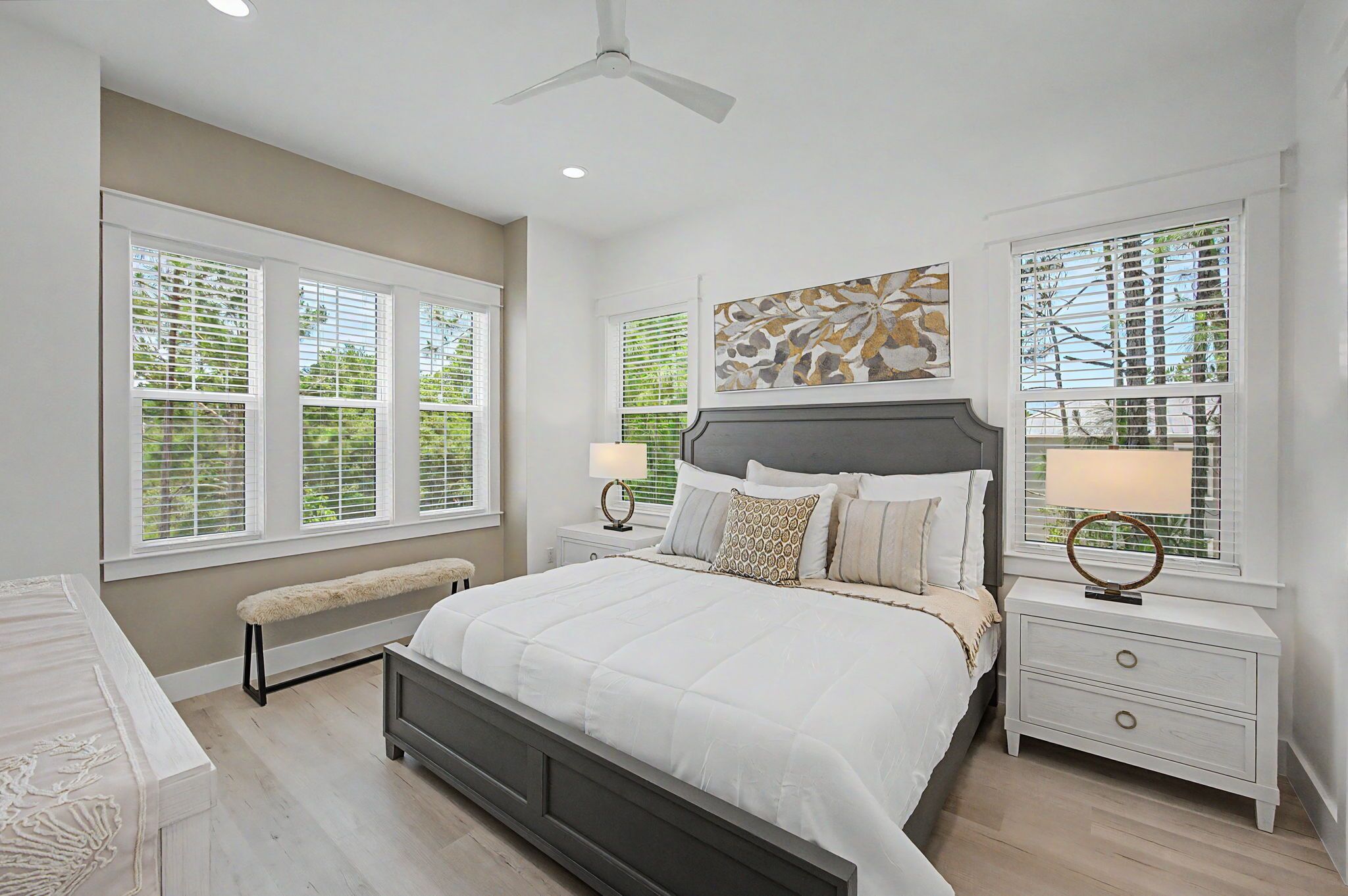 A bedroom with a bed, two bedside tables, a bench, and a ceiling fan.