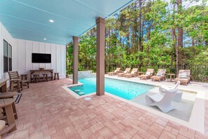 Ein überdachter Außenbereich mit Pool, Liegestühlen und einem Tisch mit Stühlen.