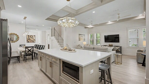 A spacious kitchen with a large island, a dining area with chairs, a staircase, and a living area with a sofa and TV. - Aquarius! New 30A Beach Home with Pool, and Golf Cart. Sleeps 28 (Santa Rosa Beach)