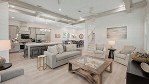 A spacious living area with a sofa, coffee table, and chairs, a kitchen with modern appliances, and a staircase leading to another level. - Aquarius! New 30A Beach Home with Pool, and Golf Cart. Sleeps 28 (Santa Rosa Beach)