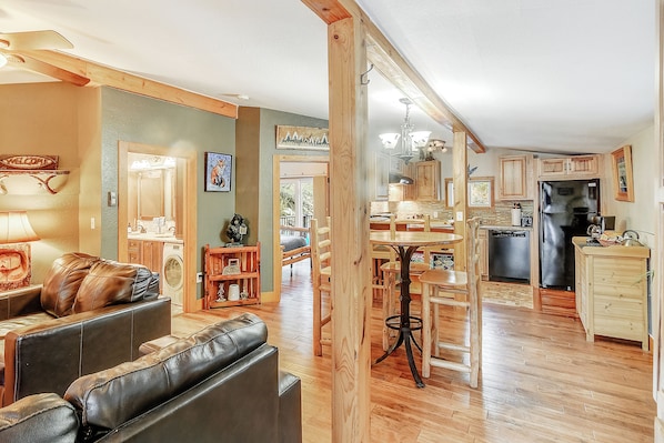 A spacious living area with a leather sofa, wooden dining table, and kitchen with wooden cabinets and appliances.