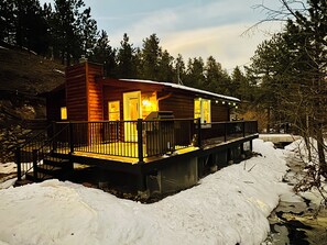 Eine Holzhütte mit einer Terrasse, umgeben von Schnee und Bäumen.
