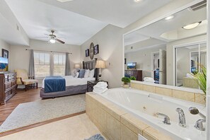 Ein Schlafzimmer mit Bett, großem Spiegel, Deckenventilator und Bad mit Badewanne und Waschbecken.