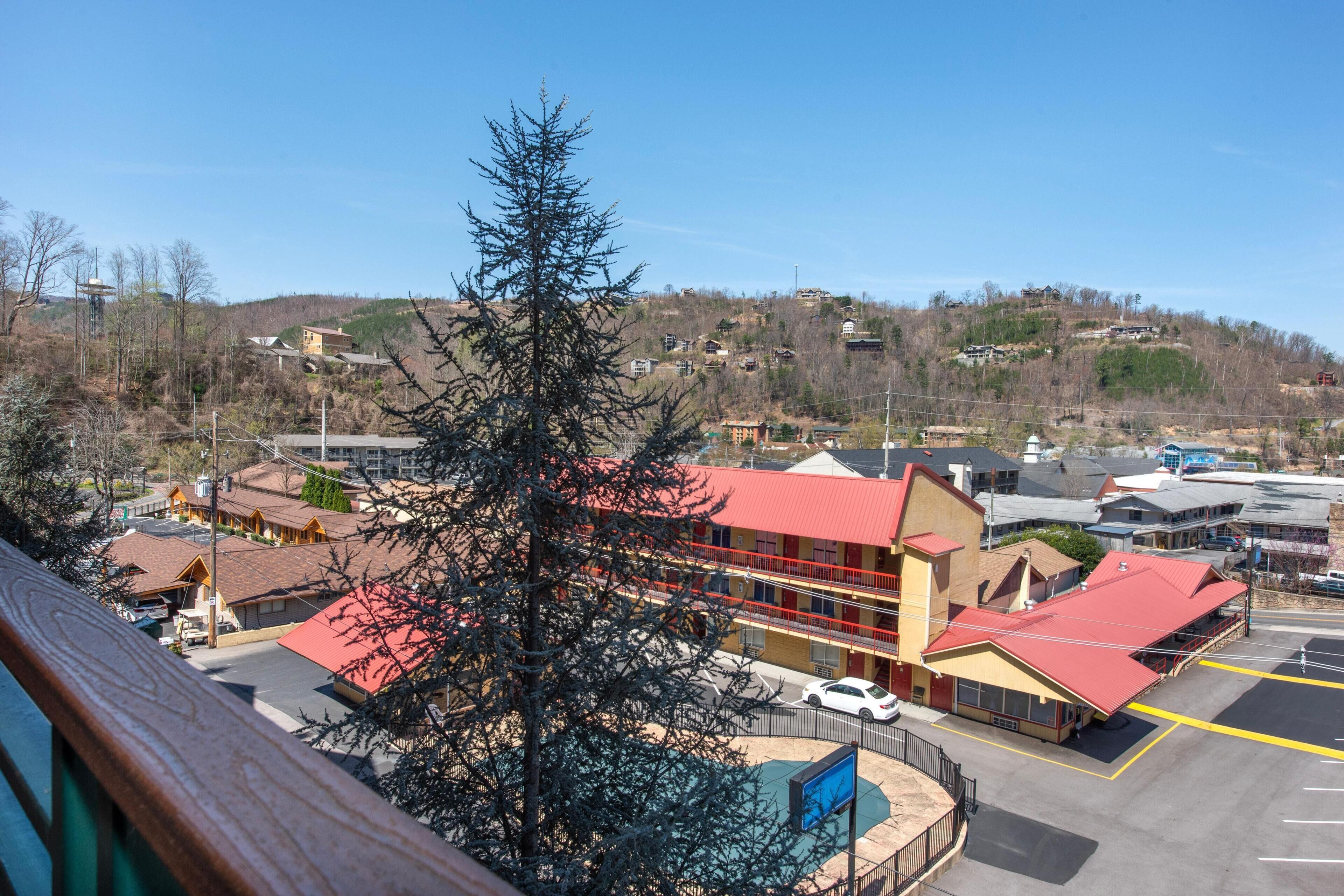 A multi-story building with a red roof, a parking lot, and a view of a hilly landscape in the background.