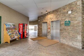 Eine Empfangshalle mit einem Coca-Cola-Automaten, einem Coca-Cola-Kühlschrank und einer Wand aus Stein mit einem Aufzug.