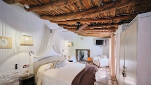 A bedroom with a wooden ceiling, a bed with a white bedspread, a bedside table, a chair, and a wardrobe. - Casa Mathilda (Fornes)