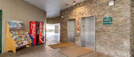 Un vestíbulo con una máquina expendedora de Coca-Cola, un refrigerador de Coca-Cola y una pared de piedra con un ascensor.
