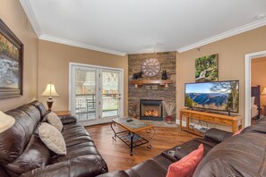 Ein Wohnzimmer mit Kamin aus Stein, Ledersofas, einem Fernseher und einer Tür, die nach draußen führt.