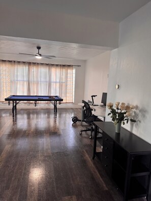 A room with a pool table, a ceiling fan, a desk with a chair, and a window with curtains. - Spacious 4 bedroom house, 15 mins from Beach, FLL Airport & Hardrock (Plantation)