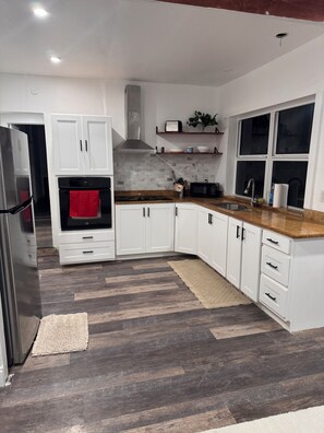 A modern kitchen with white cabinetry, a stainless steel refrigerator, a black oven, and a microwave. - Spacious 4 bedroom house, 15 mins from Beach, FLL Airport & Hardrock (Plantation)