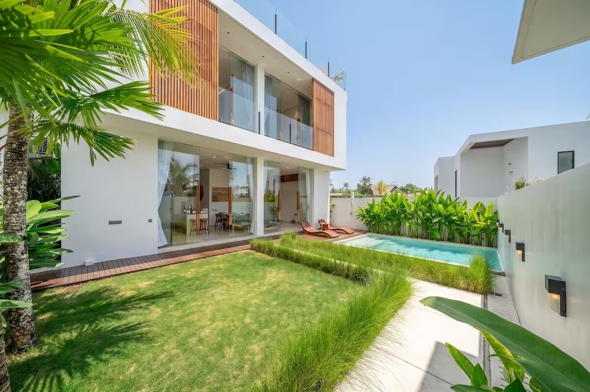 A modern two-story house with a swimming pool, a well-maintained lawn, and tropical plants.