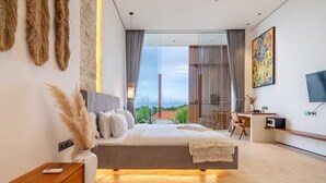 A modern bedroom with a large bed, a bedside table, a TV, and a view of the outdoors. - Karma 3 Villa (Badung)