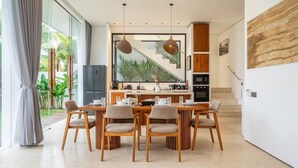 A modern kitchen with a dining area, large windows, and a staircase leading to an upper level. - Karma 3 Villa (Badung)