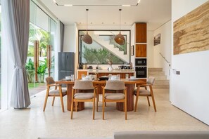 A modern kitchen with a dining area, large windows, and a staircase leading to an upper level. - Karma 3 Villa (Badung)