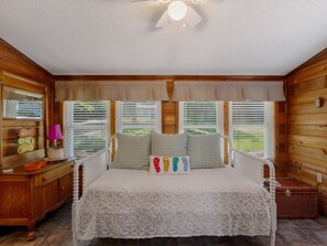 Ein Schlafzimmer mit Bett, Schminktisch, Nachttisch, Lampe und einem Fenster mit Jalousien.