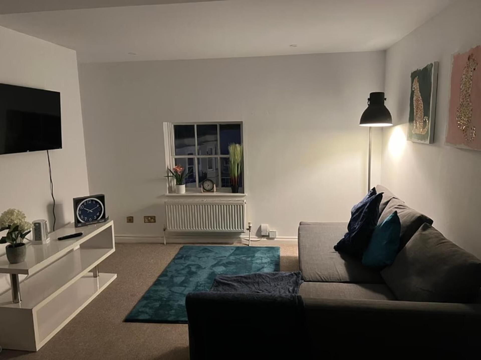Una sala de estar con sofá, televisión, radiador, ventana y lámpara.